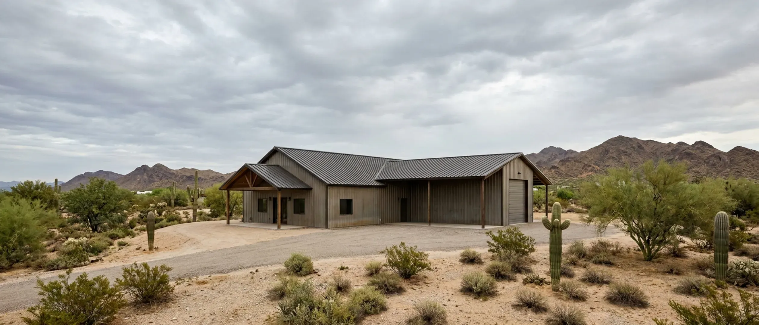 A completed barndominium with a covered entry porch and an attached shop bay on desert acreage under high clouds.
